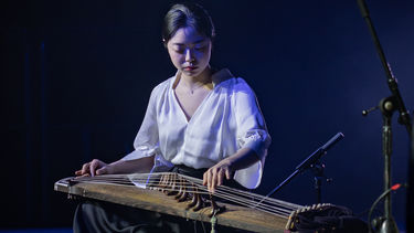 A woman dressed in white playing a Japanese Koto onstage. 