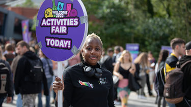 A person with short bleached hair holding up a sign that reads: 'Activities fair today!'