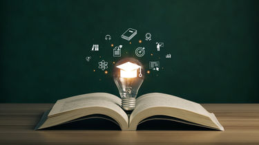 An open book with a lit lightbulb wedged inside it with various icons floating around it relating to different academic subjects