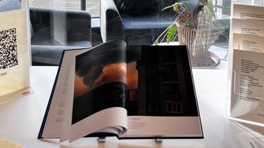 A table with an open book on which a photot of a destroyed city at sunset is shown plus leaflets with poems on
