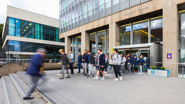 Large group of students leaving the Arts Tower, while a person moving quickly (blurred) walks towards them