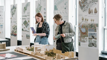 Two people pointing and discussing a display/model