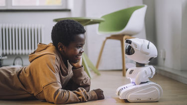 A little boy lying on the floor looking at a small robot
