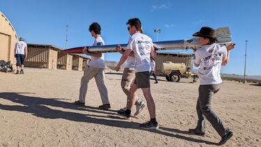 Three students carrying the Desert Winds rocket through the US desert