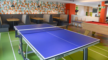 A common room with a ping pong table and booths