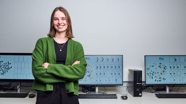 Maisy Wilkes, winner of the the 2024 Chancellor's Medal Award sat in front of computers showing genetics research.