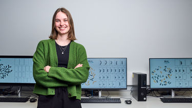 Maisy Wilkes, Sheffield alumni, smiling at the camera in front of computers.