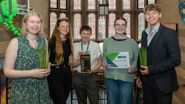 5 members of the FOSS Green Impact team, posing with a certificate, award and two plants. 