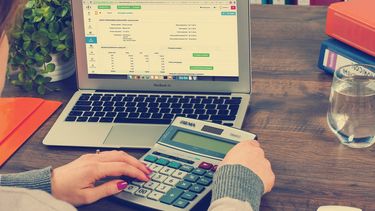 A person checking figures on a computer with a calculator.