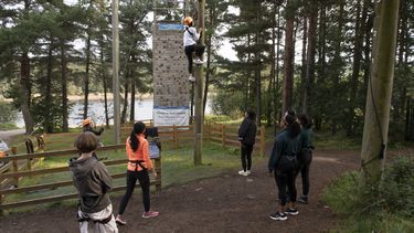 A student climbing a high ropes course with others watching on.