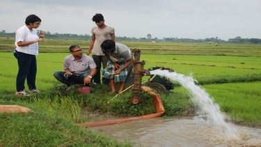 Scientists conduct fieldwork, speaking to a farmer by an irrigation pump
