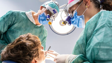 Dental student examines a patient's mouth as another dentist watches