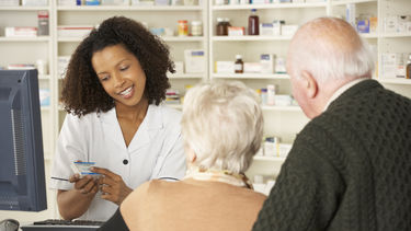 A pharmacist in a white coat talks to an elderly couple