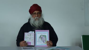 An older man holds up pieces of Art, he sits in front of a screen reading 'Thriving Together: A symposium on couplehood, arts participation and dementia. 