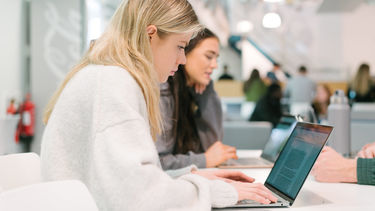 Two female students looking at laptops in a study space