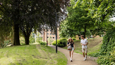 Two students walking down a path through a leafy accommodation site