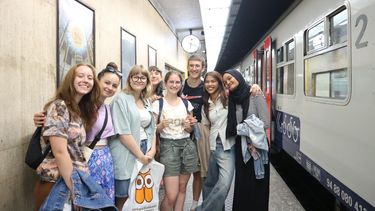 group of eight young people on a station platform. Belgian train is visible on the right