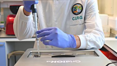 A person in a labcoat with the logo of the Clinical Infection Research Group (CIRG) uses lab equipment