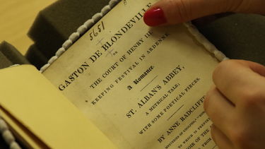 A close up of a woman holding the title page of Gaston de Blondeville