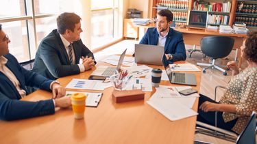 4 lawyers sit round a table in a big office