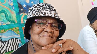 A woman in glasses and a leopard print hat smiling at the camera