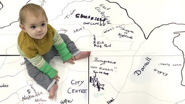 Photograph of small child sitting on a hand drawn map of Sheffield written in different languages
