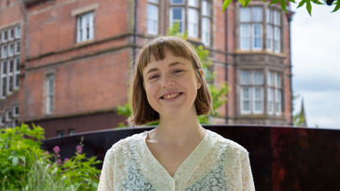 Person with short hair smiling standing in front of University building