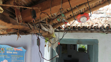 A solar lamp is attached to a roof beam with a tangle of wires