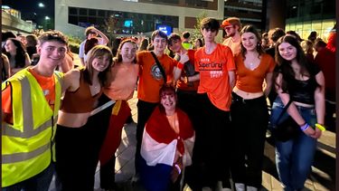 night scene with students, one in a high viz jacket and most dressed in orange, on a night out