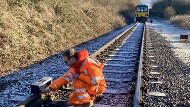 Man on a railway track holding device on the rails in front of bridge