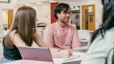 Three Sheffield management students working together at a table with their laptops and notebooks