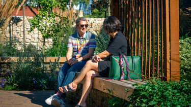 Two people sat on a bench in a green pocket park on a sunny day