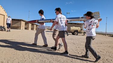 Four students carrying a rocket in a desert