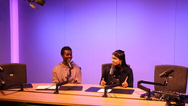 Two women sat at desk with microphones recording a podcast