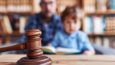 Photo with a gavel at the forefront and a blurred image of a father and son in the background