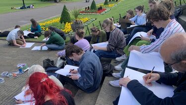 students sitting on a staircase outside Weston Park Museum all drawing on large pads. colourful beds of flowers in the background