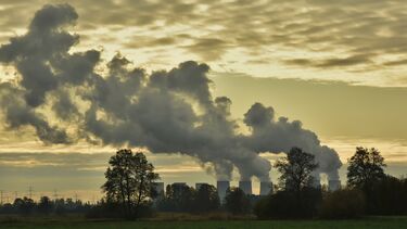 A field with smoke coming out of chimneys in the background.