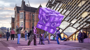 Image shows students interacting with a large purple fortune telling cube outside the Diamond build. The cube features words and phrases like University of the Year, Russell Group and No 1 Students' Union.