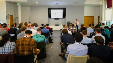 View of a doctoral researcher presenting to a full room 