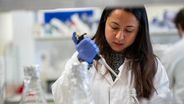 A person in a lab, wearing a lab coat, carrying out scientific tests.