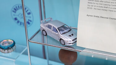 A museum display with a silver toy car on the shelf. 