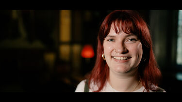 Rebecca Raven smiling against the backdrop of a dimly-lit museum room