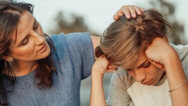Photograph of a woman comforting a sad looking young adult