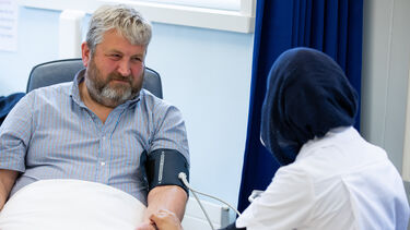 Med student in a headscarf holds the arm of a patient wearing a blood pressure cuff.