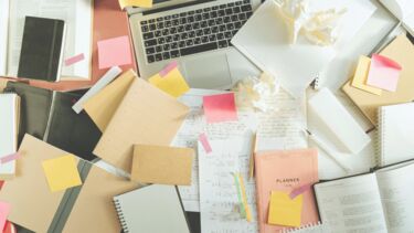 A messy desk with a laptop, crumpled notes and papers. 