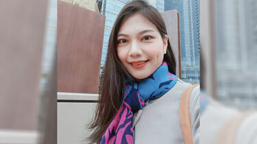 Shelley Tien wearing a coloured scarf and standing in front of a skyscraper