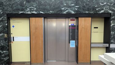 A passenger lift with wood panels at either size and a door to the left and book return lift to the right