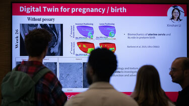 Silhouttes of people talking in front of a large screen displaying a research slide