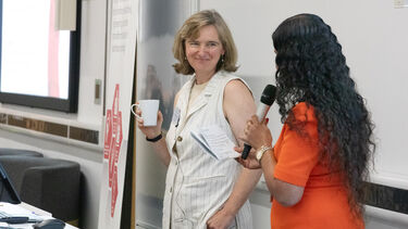 Two women standing looking at each other, one holding a cup the other holding a microphone