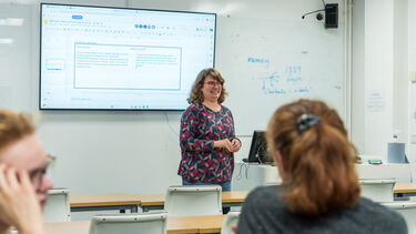 A lecturer stood at the front of a lecture theatre smiling at the students